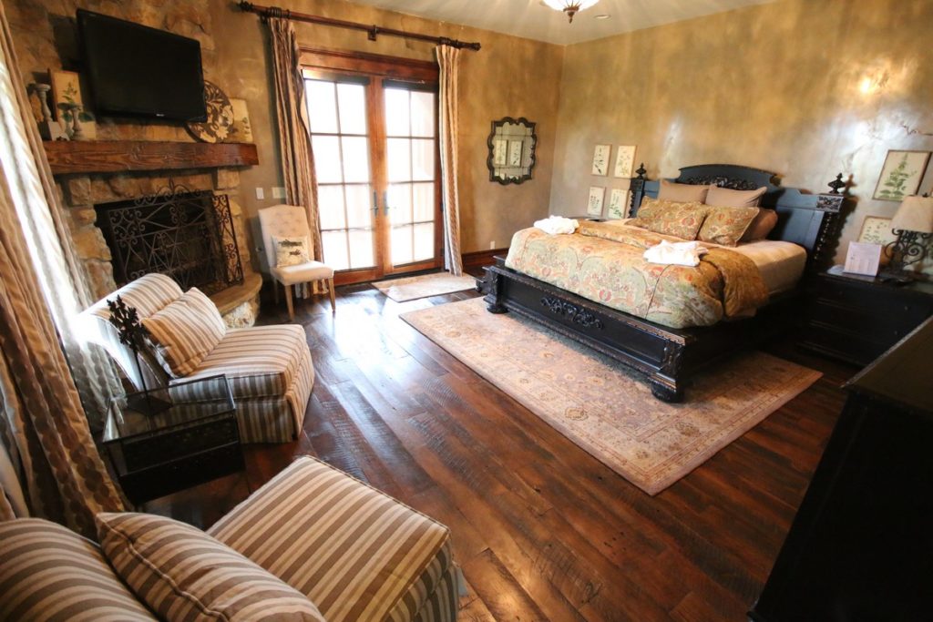 Bedroom with king bed, two large stuffed chairs, TV and fireplace